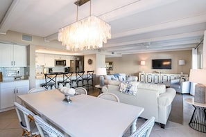 Ein modernes Wohnzimmer mit einem weißen Sofa, einem Esstisch mit Stühlen und einer Küche im Hintergrund.