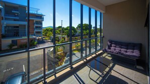 A modern room with large windows, a sofa, and a view of a building and greenery outside. -  1 bdrm  apartment  roof top pool, gym, mountain views, 24 hr security  Barbican (Kingston)
