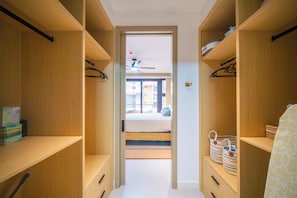 En smal hall leder in till ett sovrum med en säng, hyllor i trä och en takfläkt.