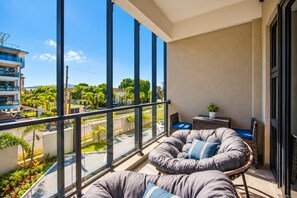 Ein Balkon mit großen Fenstern, einer gepolsterten Sitzecke und einem kleinen Tisch mit einer Pflanze.