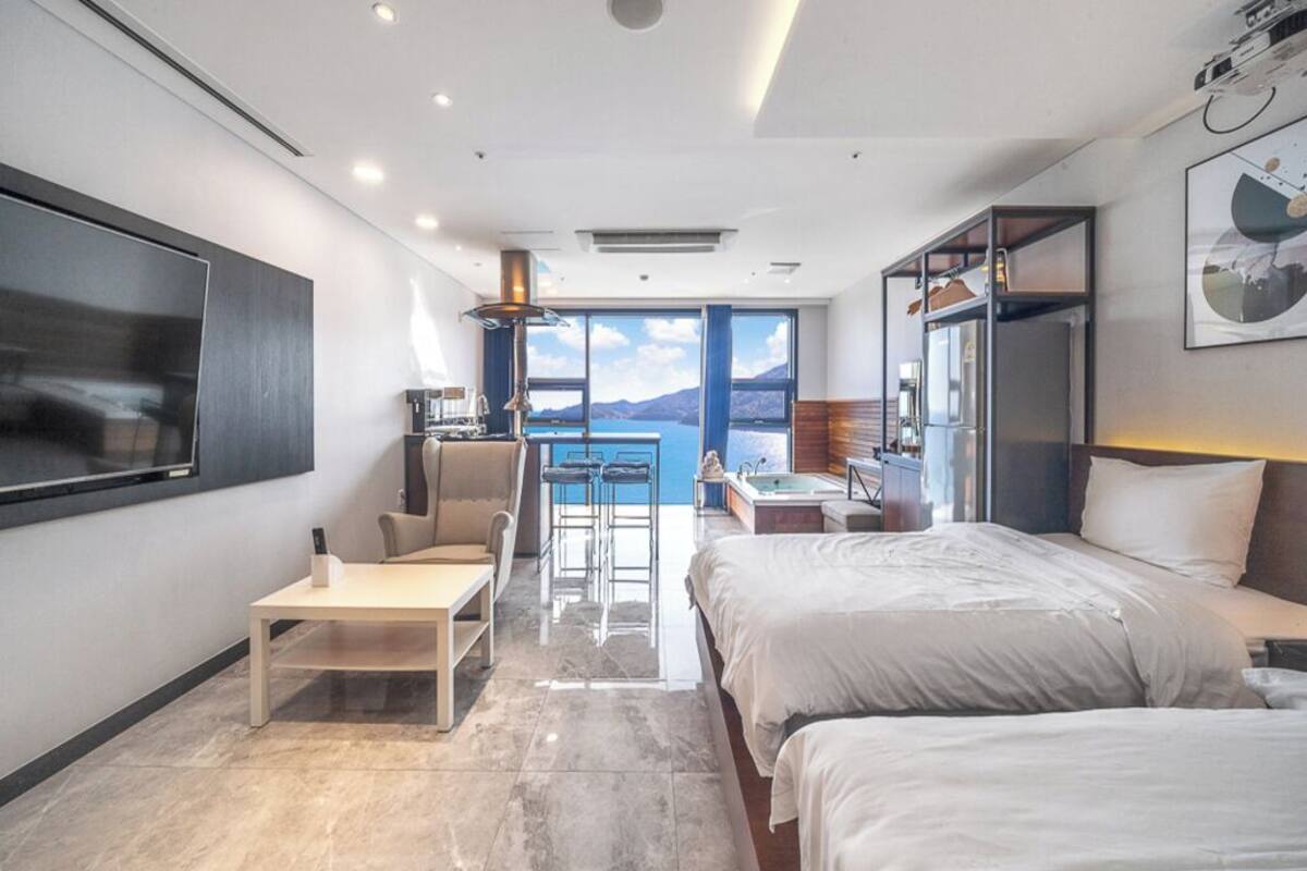 A modern hotel room with a large bed, a desk, and a seating area with a view of the sea.