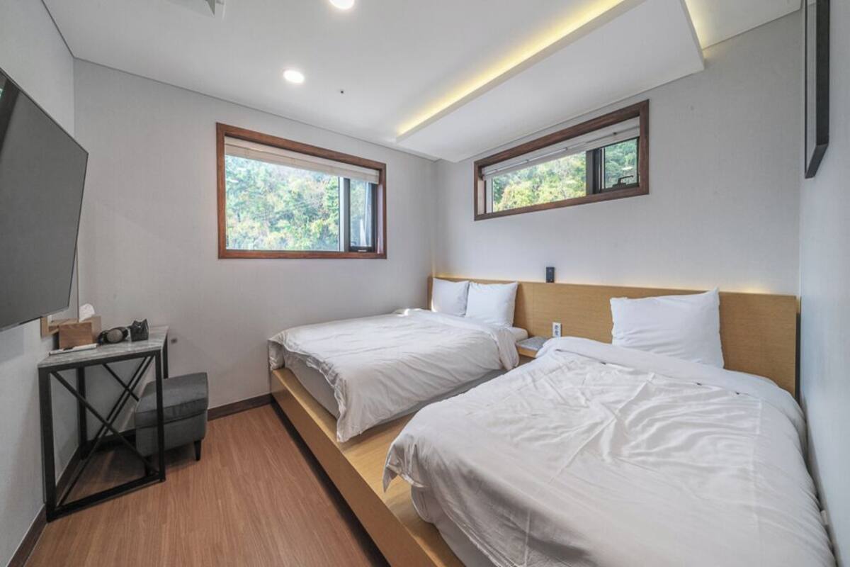 A hotel room with two beds, a small table, and a window.