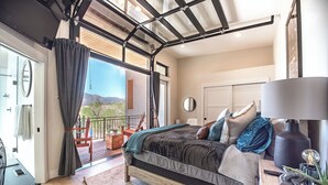 Una camera da letto con un letto, un comodino, una lampada, una finestra e vista sull'esterno.