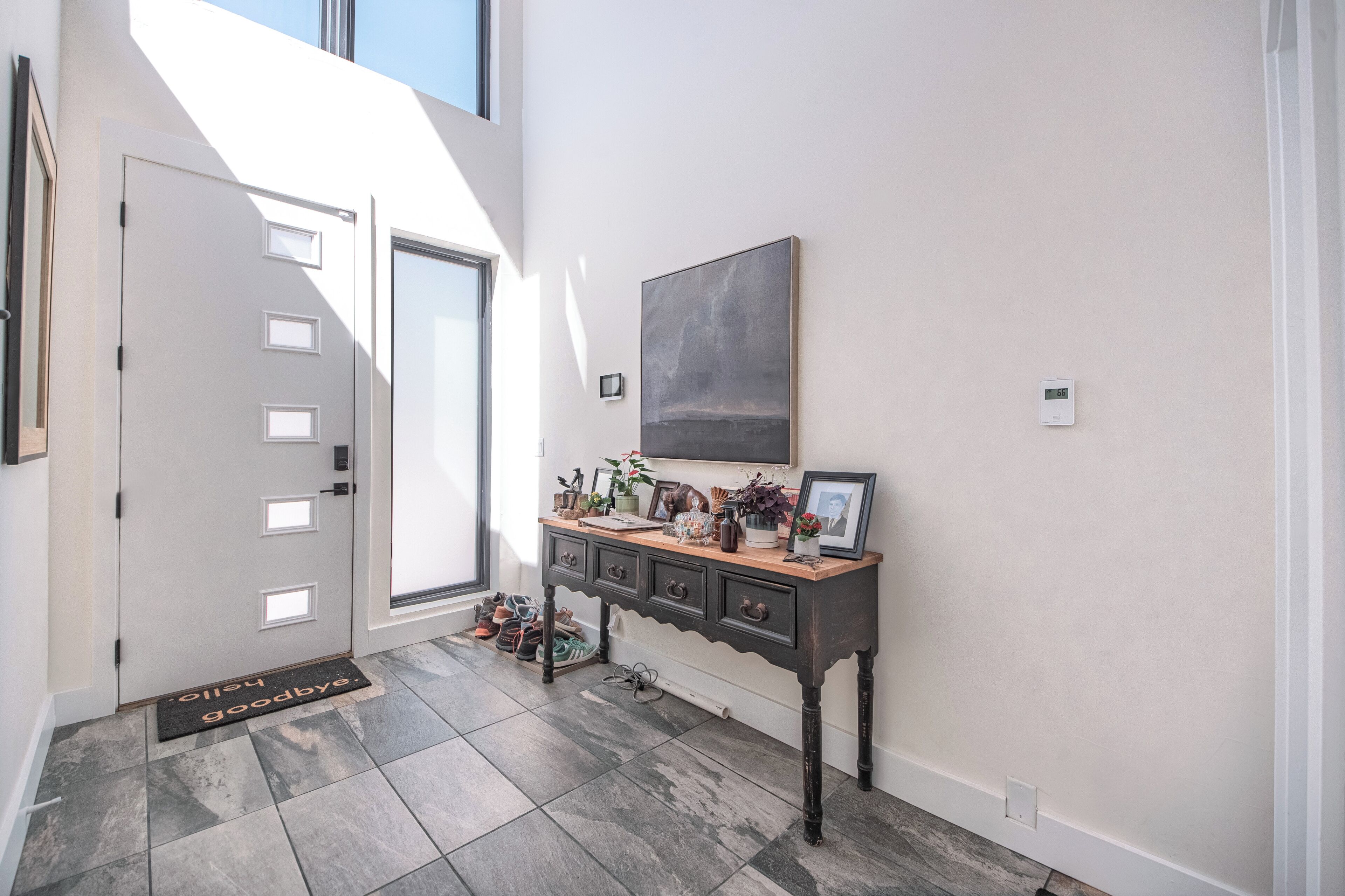 A hallway with a door, a console table with decorative items, a large abstract painting, and a doormat.