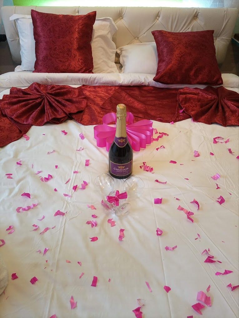 A bed with a white bedspread, a bottle of champagne, and scattered rose petals.