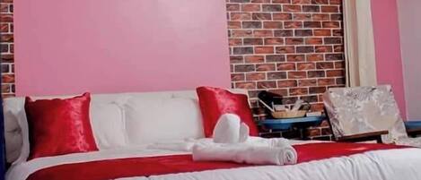 A bedroom with a brick-patterned accent wall, a painting above the bed, and a pair of slippers on the floor.