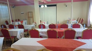 Une salle de conférence avec plusieurs tables et chaises, des bouteilles d’eau sur chaque table et une porte au fond.