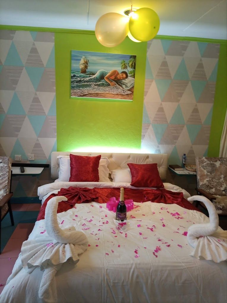 Un lit parsemé de pétales de rose et une bouteille de champagne, un tableau accroché au mur et un mur orné d’un motif géométrique.
