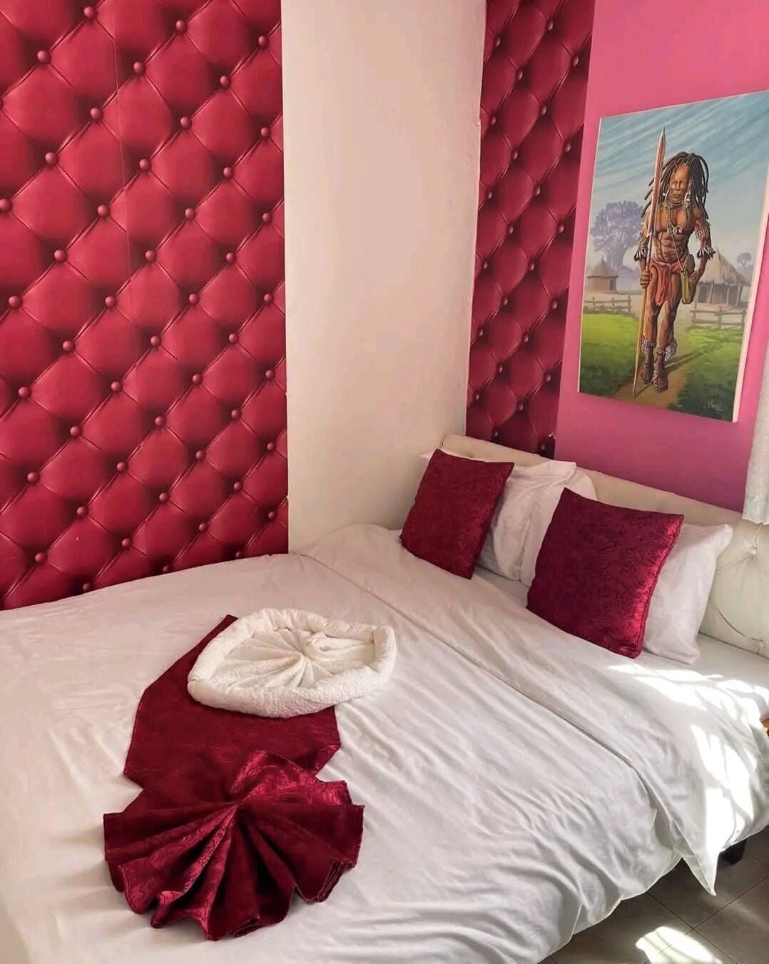 Quarto com cabeceira estofada, roupa de cama branca e manta vermelha.