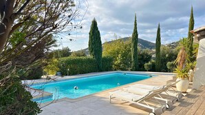 Una piscina rettangolare con acqua cristallina e azzurra, circondata da un solarium in legno e lettini.
