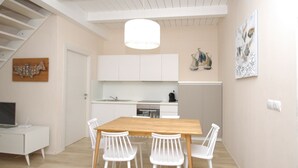 A modern kitchen with white cabinets, a wooden dining table, and white chairs. - MARINAZZURRA  - Goelba (Porto Azzurro)