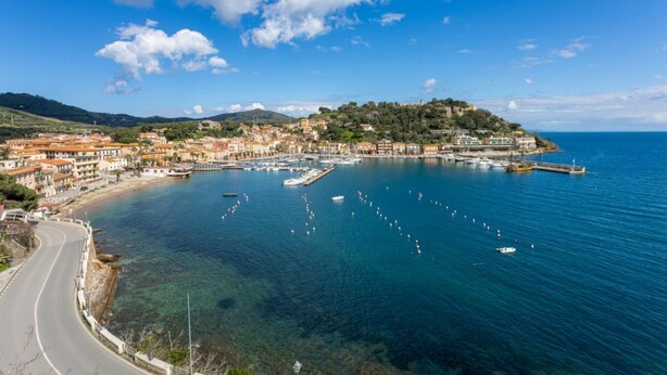 A coastal town with a marina, clear blue sea, and buildings along the shore. - MARINAZZURRA  - Goelba (Porto Azzurro)