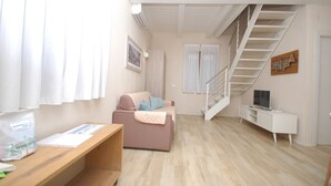 A modern living room with a sofa, a TV, a staircase, and a desk with papers. - MARINAZZURRA  - Goelba (Porto Azzurro)