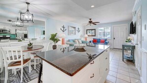 A spacious kitchen with white cabinetry, a central island, and a dining area with white chairs. - Street Legal Golf Cart Included! Park right at the front door. (Panama City Beach)