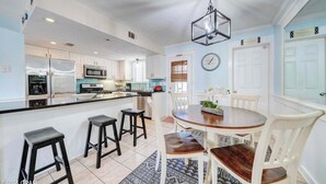 A modern kitchen with white cabinets, a stainless steel refrigerator, and a central island with stools. - Street Legal Golf Cart Included! Park right at the front door. (Panama City Beach)