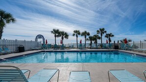A swimming pool with blue lounge chairs and red umbrellas, surrounded by a white fence and palm trees. - Street Legal Golf Cart Included! Park right at the front door. (Panama City Beach)