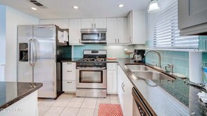 A modern kitchen with stainless steel appliances, white cabinets, and a granite countertop. - Street Legal Golf Cart Included! Park right at the front door. (Panama City Beach)