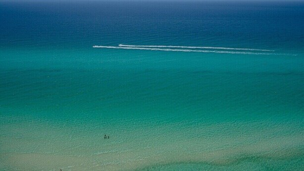An aerial view of a beach with clear turquoise waters and a visible wake from a boat. - Street Legal Golf Cart Included! Park right at the front door. (Panama City Beach)