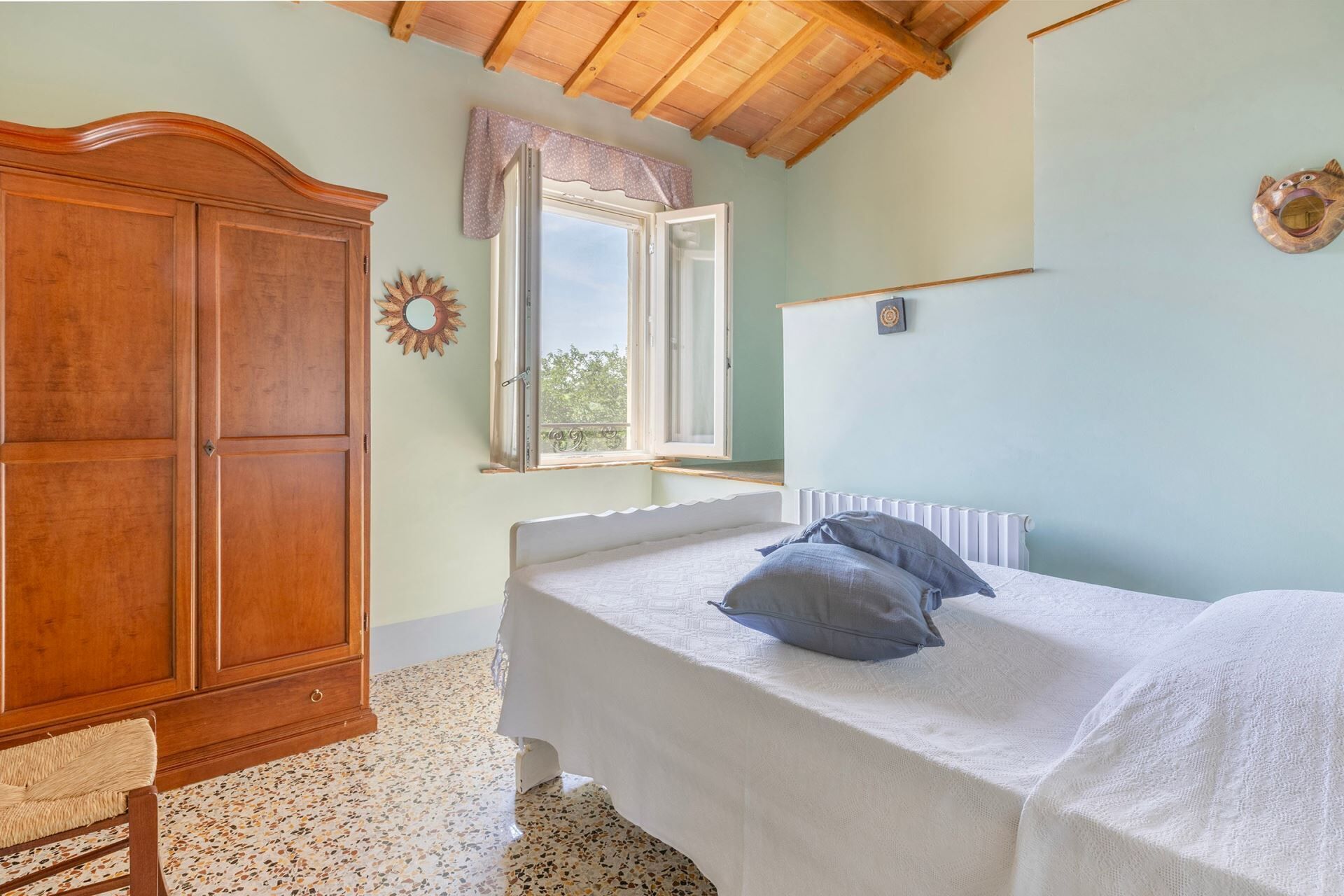 A bedroom with a bed, a wooden wardrobe, a window with a view, and a radiator.