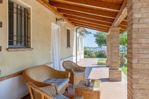 A covered outdoor area with wicker furniture and a table, a brick pillar, and a view of a garden.