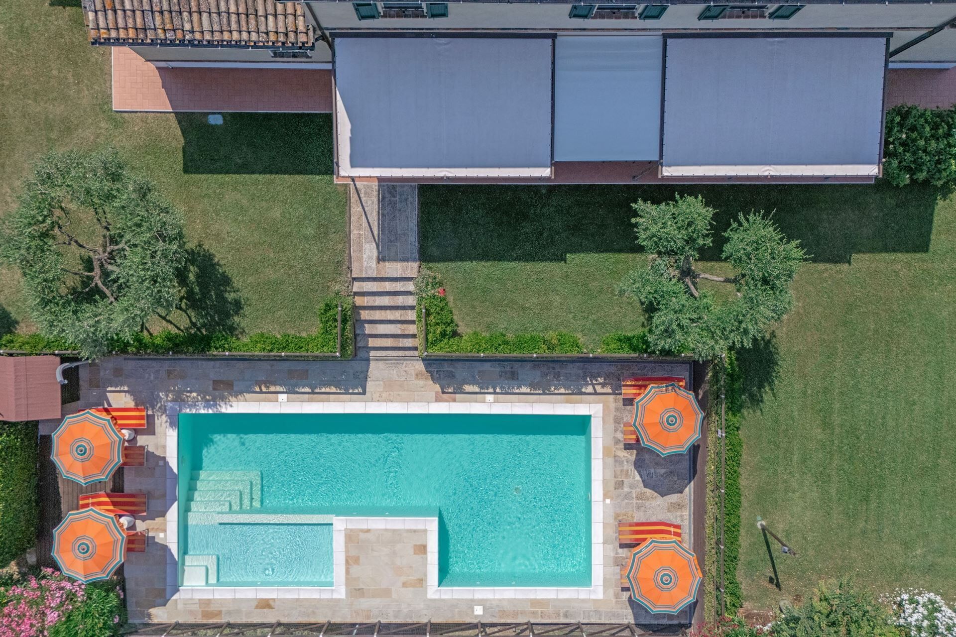 An aerial view of a swimming pool with adjacent lounge chairs and a covered area.