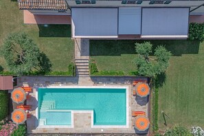 An aerial view of a swimming pool with adjacent lounge chairs and a covered area.