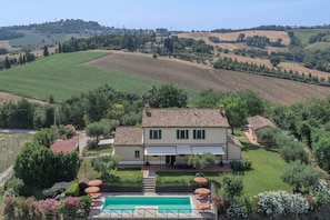 A villa with a swimming pool, surrounded by lush gardens and fields.