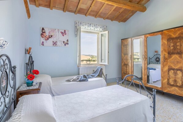 A bedroom with two beds, a window with a view, a wooden wardrobe, and a mirror.