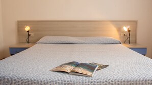 Een net opgemaakt bed met een bedsprei met patroon, twee nachtlampjes en een tijdschrift op het bed.