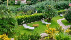 Een weelderige tuin met twee ligbedden, een kiezelpad en diverse beplanting, waaronder palmbomen en struiken.