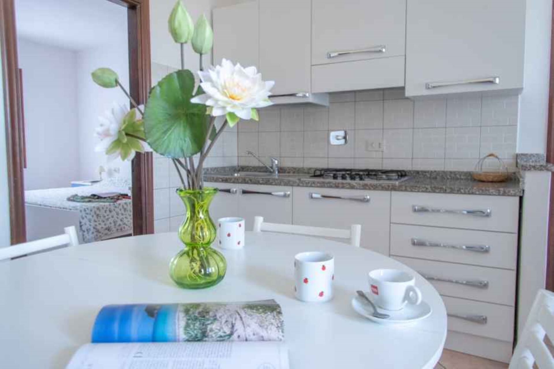 A kitchen with white cabinets, a granite countertop, and a dining table with a vase of flowers.