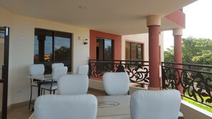 Un balcon avec des chaises blanches et une table, une balustrade et une vue sur les arbres et les bâtiments.