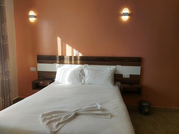 Una cama bien hecha con sábanas blancas, dos mesitas de noche con lámparas y una lámpara de pared.