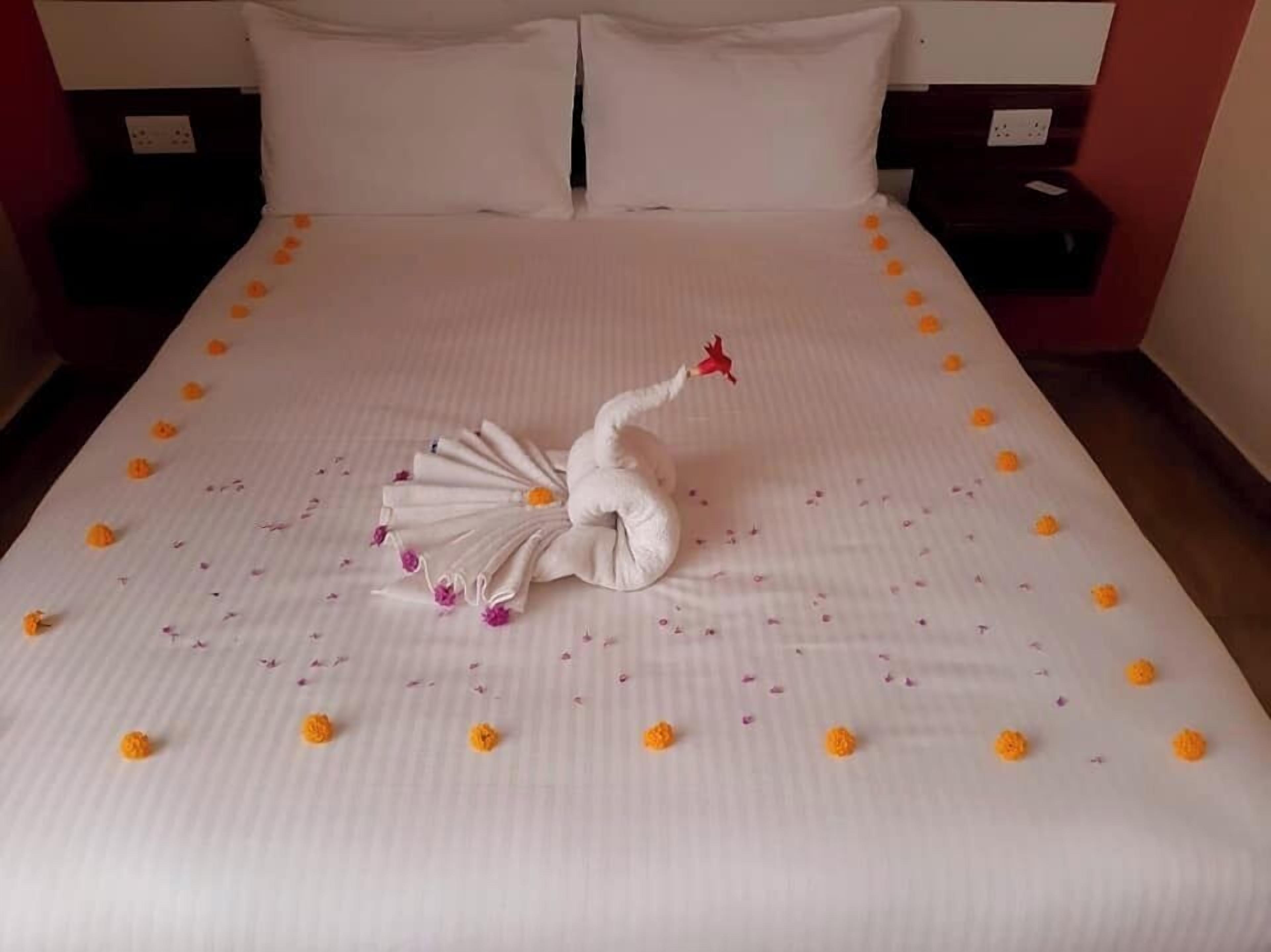 A neatly made bed with a swan-shaped towel and orange flowers.