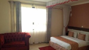 Une chambre d’hôtel avec un lit, un fauteuil rouge et une fenêtre avec des rideaux.