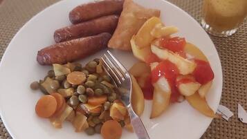 Un plato de comida con salchichas, un alimento frito, verduras mezcladas y un vaso de jugo sobre una mesa.