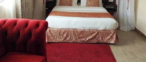 A bedroom with a large bed, two bedside tables, a red sofa, and sheer curtains with a red trim.