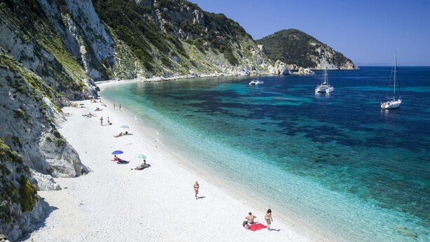 Een strand met helder turquoise water, rotsachtige kliffen en boten.