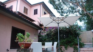 Een terras met een tafel, stoelen, een bloempot en een grote parasol.