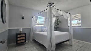 Een slaapkamer met een hemelbed, een nachtkastje met een lamp en een raam met zonwering.