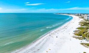 A beach with a wide sandy shore, clear blue water, and a few buildings in the background. - Sarasota Paradise Near Siesta Key (3709) (Sarasota)
