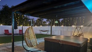 Een overdekte buitenruimte met een jacuzzi, een hangstoel en lichtjes.