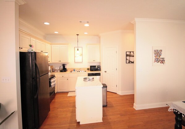A modern kitchen with white cabinetry, a black refrigerator, a microwave, and a central island. - LUX Home, 3min from LSU, KING Bed (Baton Rouge)