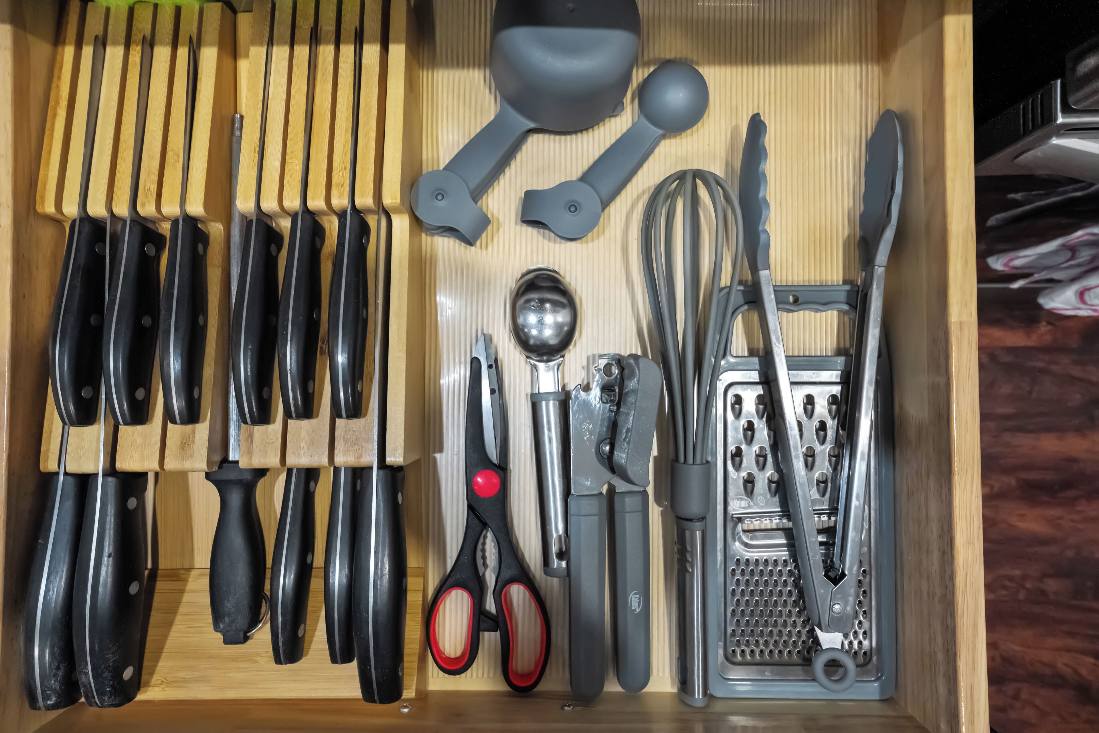 A drawer with various kitchen utensils including knives, scissors, and a grater.