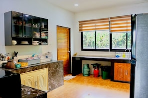 A kitchen with a marble countertop, a black cabinet with glass doors, a wooden door, a window with blinds, and a sink.