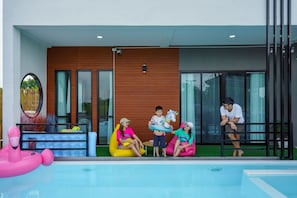A modern building with a pool area, featuring a wooden wall, glass doors, and a seating area with colorful bean bags.