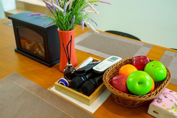 A table with a small black heater, a vase with lavender, a basket of apples and oranges, and a wooden box with microphones.