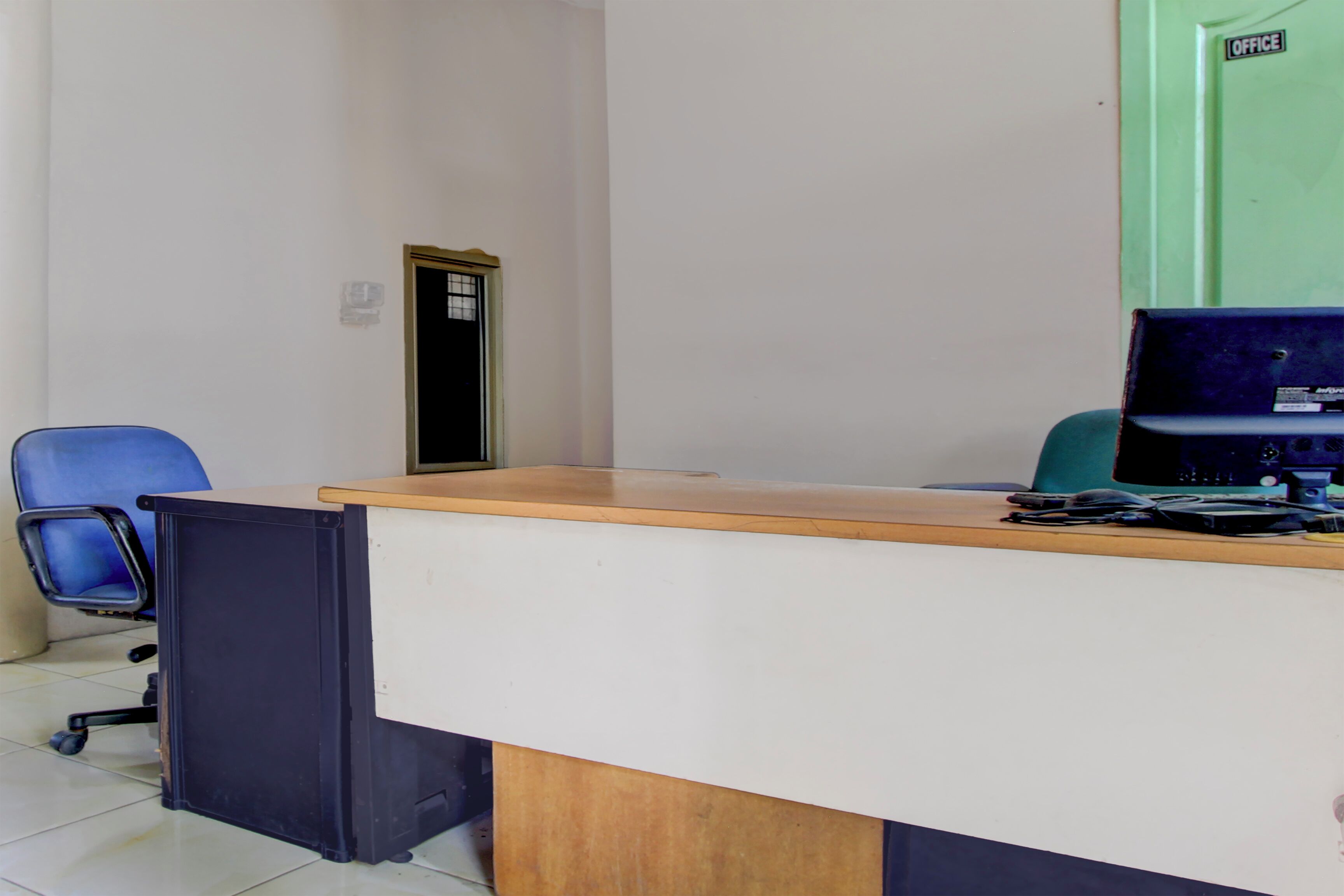 Una habitación con un escritorio, una silla, una computadora y una puerta con la leyenda “OFICINA”.