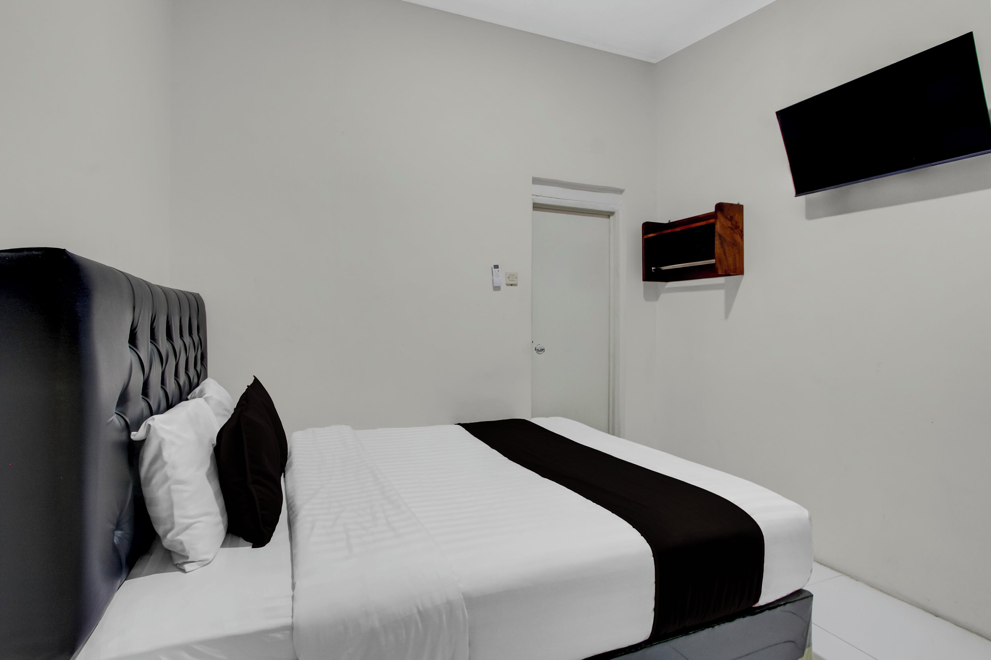 Ein Schlafzimmer mit einem Bett, Kissen, einem Nachttisch, einem flachbildfernseher an der Wand und einer Tür.
