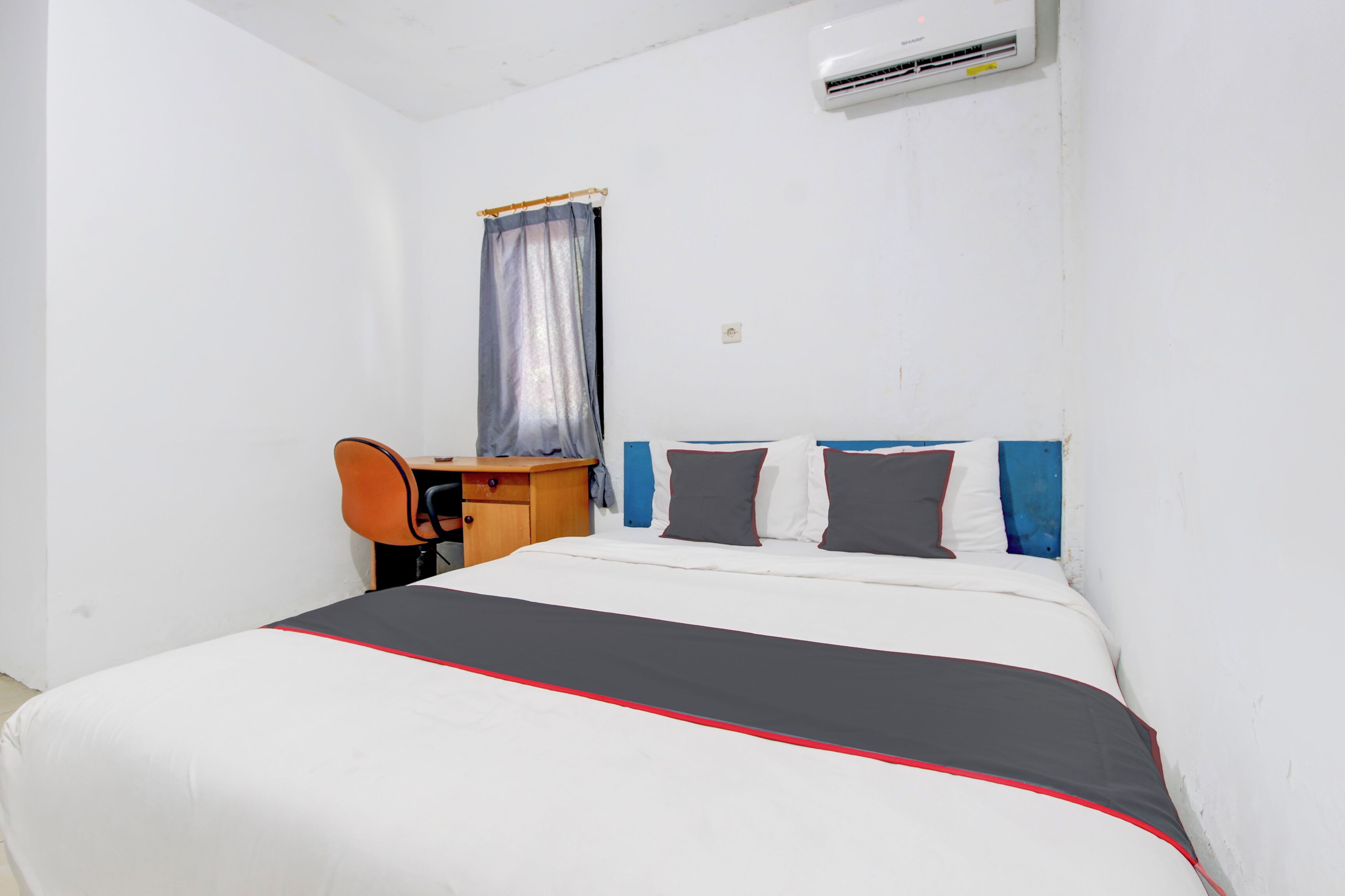 A hotel room with a bed, a desk, and an air conditioning unit.